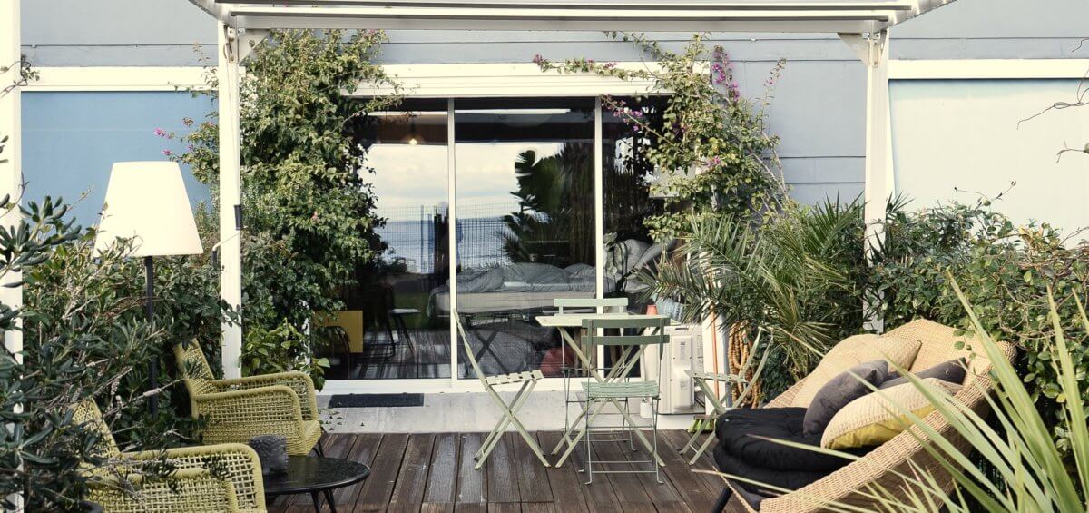 Outdoor area with plants, chairs, and pergola next to a blue house
